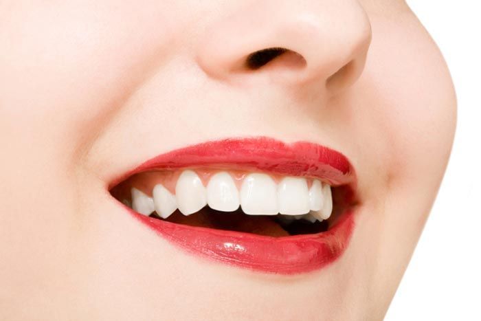 Un primer plano de la boca de una mujer con dientes blancos y lápiz labial rojo.