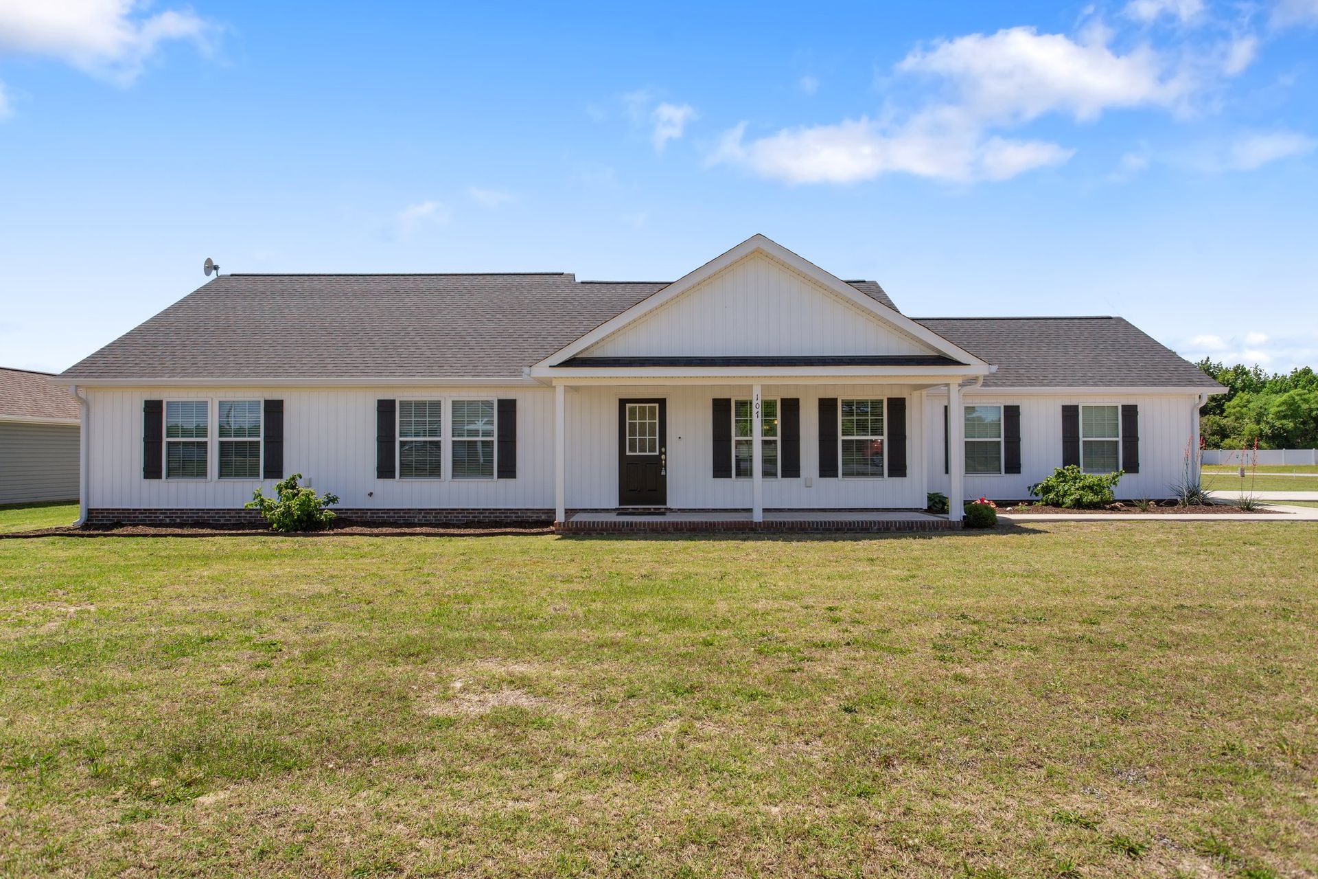 Single-story white house with a gray roof and front porch, set behind a wide grassy yard under a blue sky