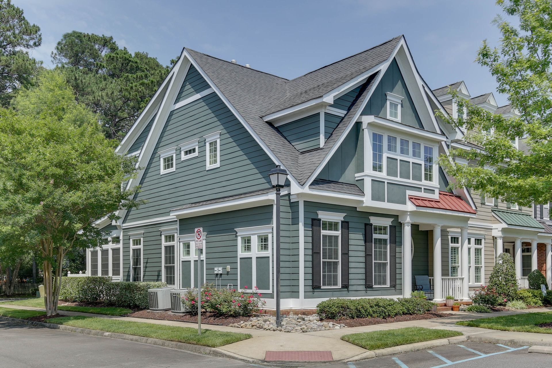 Gray-blue house with white trim, steep gables, and a red awning in a leafy neighborhood