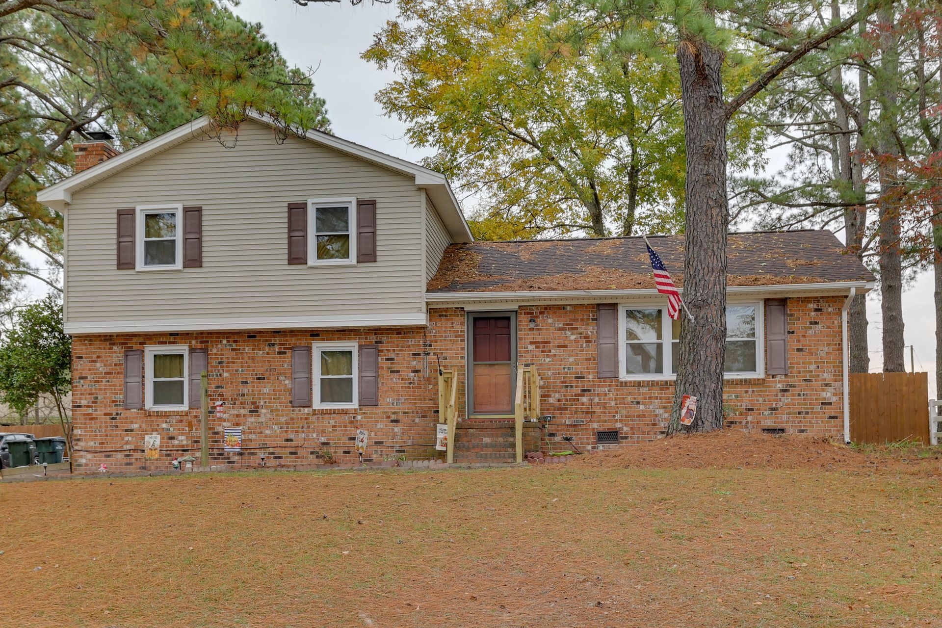 Suburban house with brick and siding exterior, trees, and a leaf-covered front yard in autumn