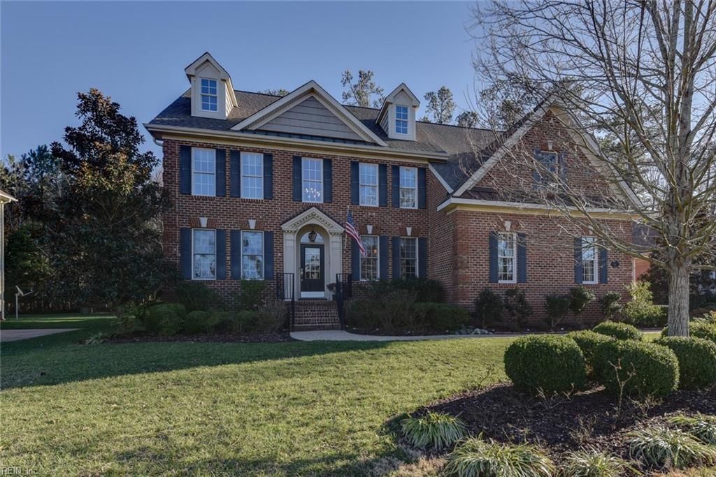 Two-story brick house with white trim and a manicured front lawn on a sunny day