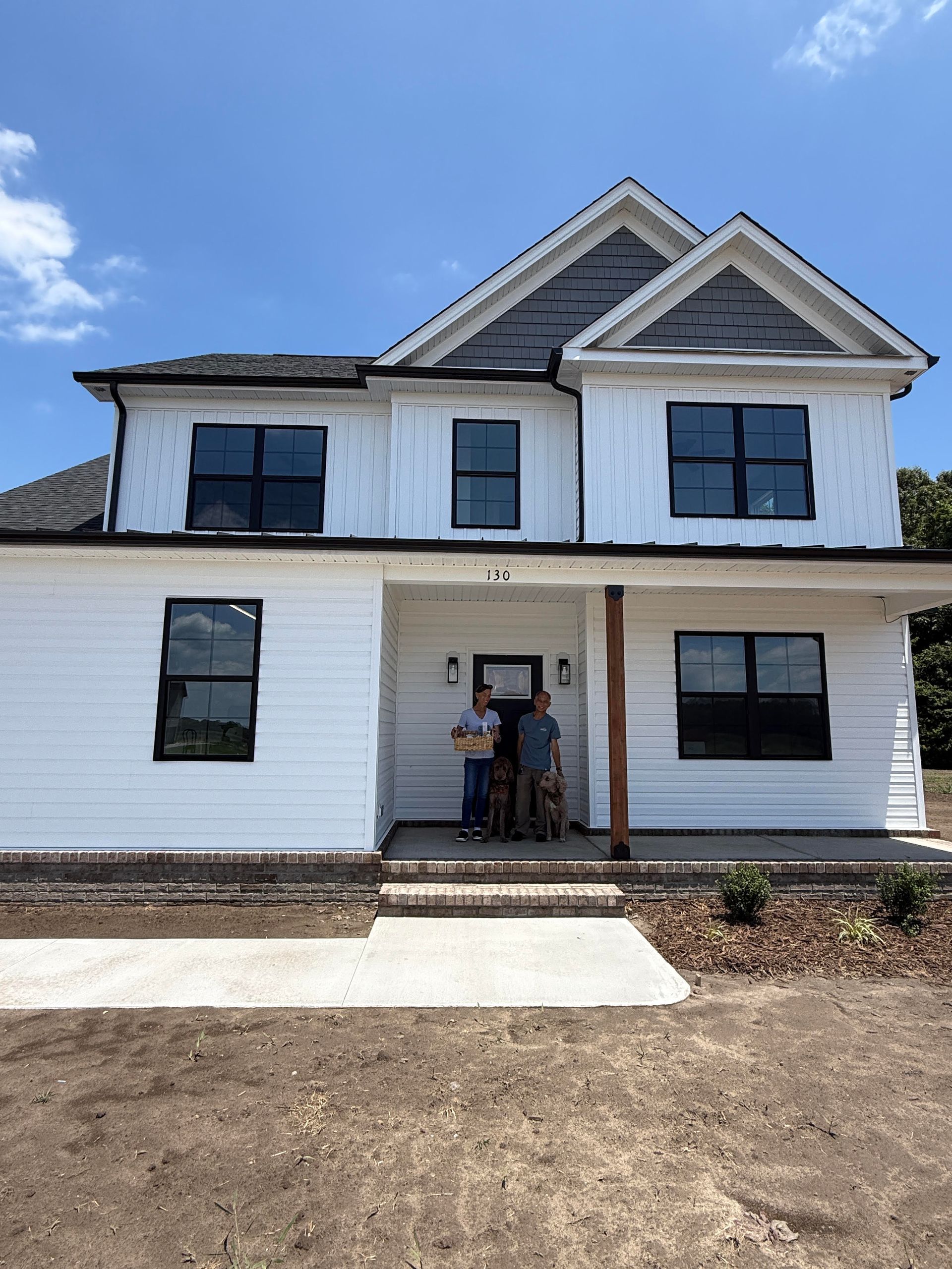White two-story house with black-trimmed windows and two people standing in the front doorway.