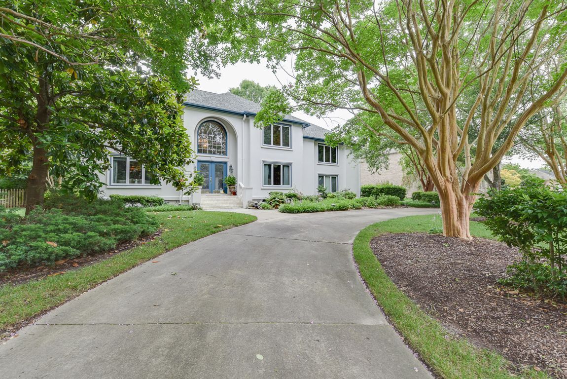 Tree-lined driveway leading to a large white two-story house with an arched entryway