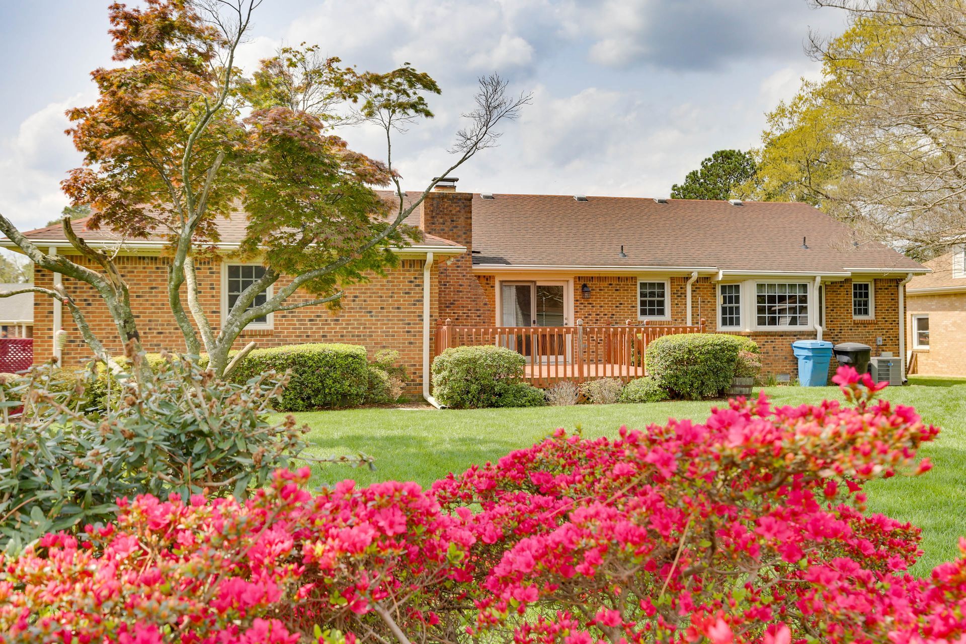 Brick house with a front porch and pink flowers in the foreground under a cloudy sky