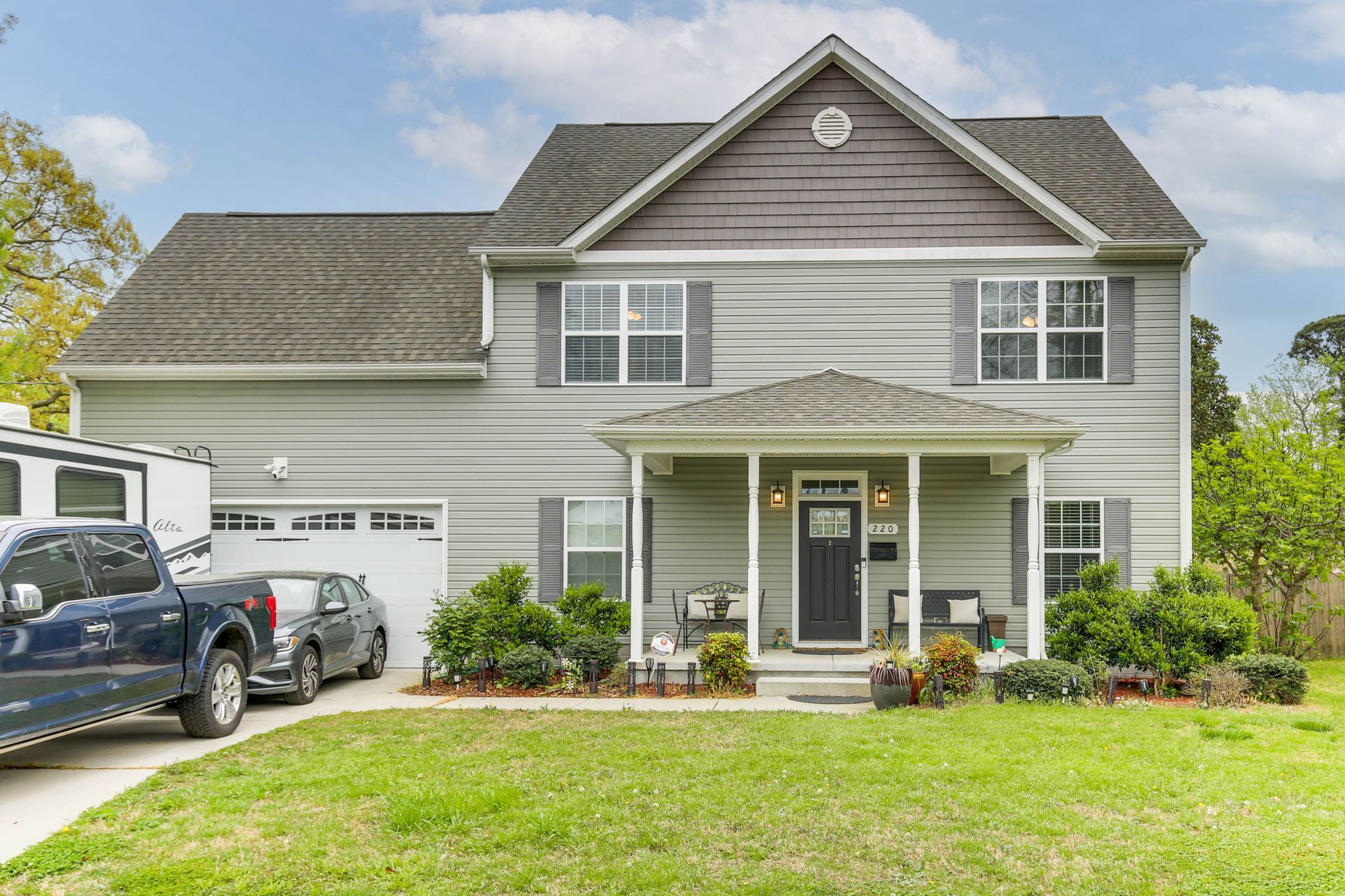 Gray two-story suburban house with a covered front porch, white trim, and parked cars in the driveway