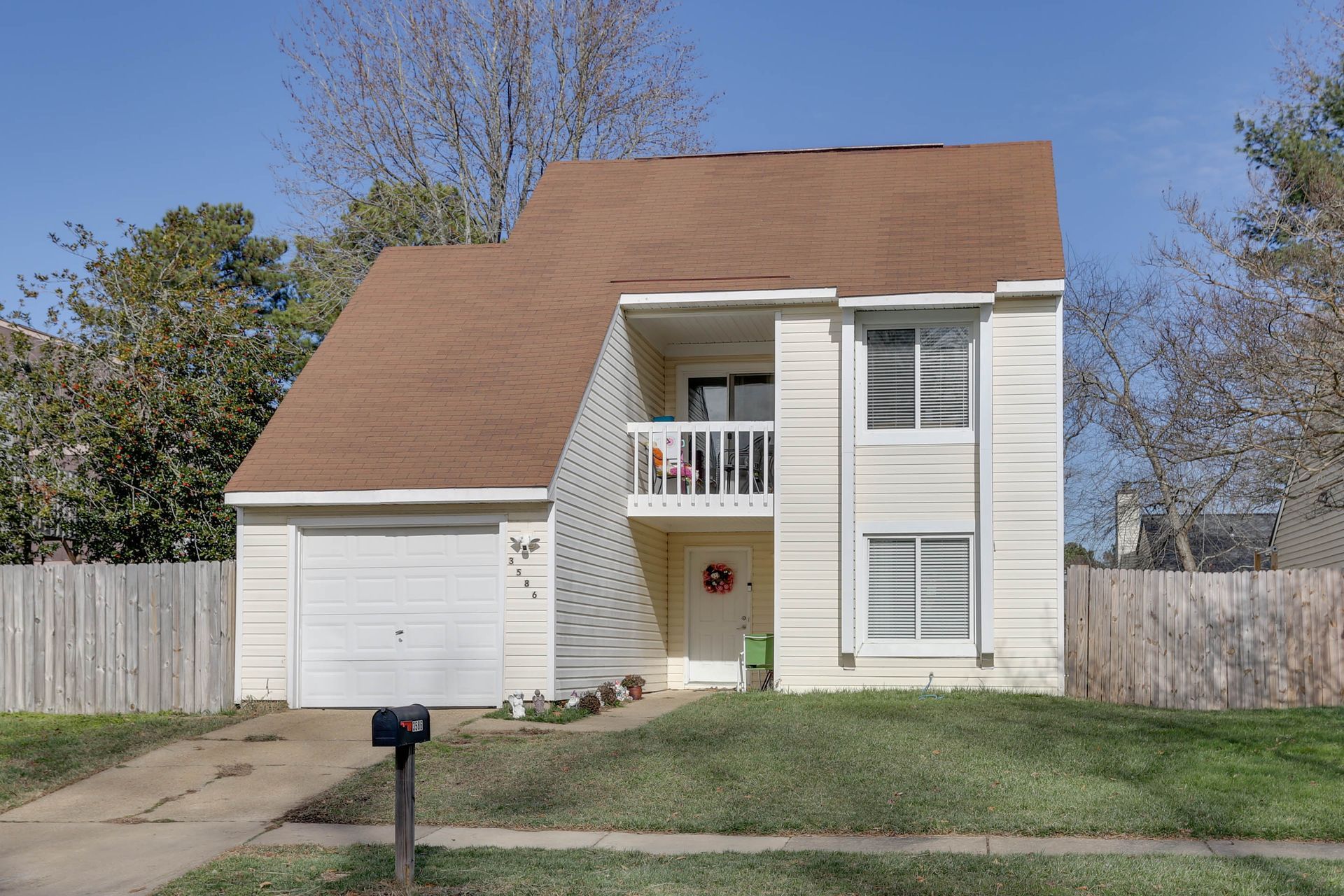 Two-story tan house with garage, white shutters, and a front lawn under a clear sky