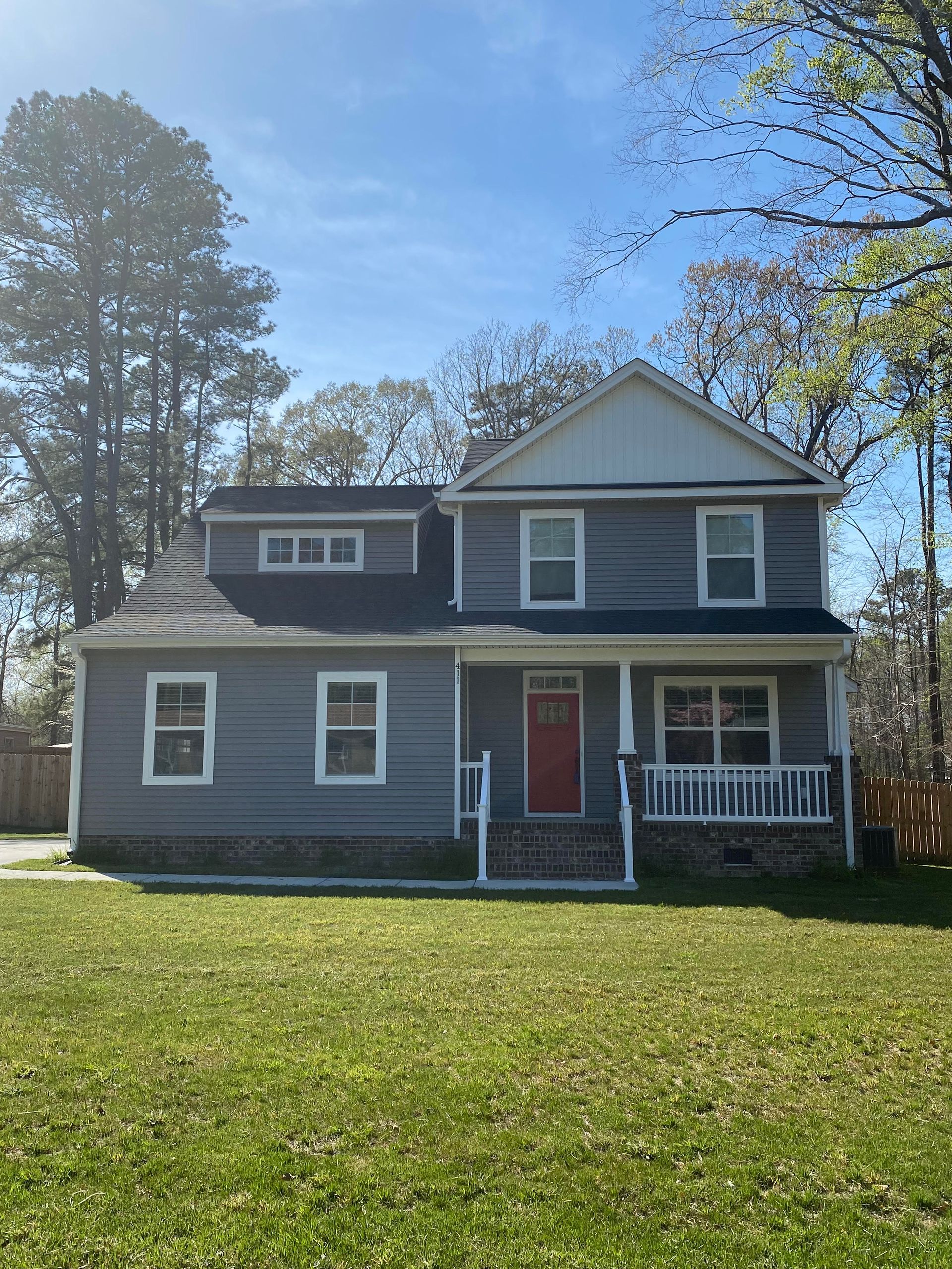 Two-story gray house with red front door and white porch on a sunny lawn
