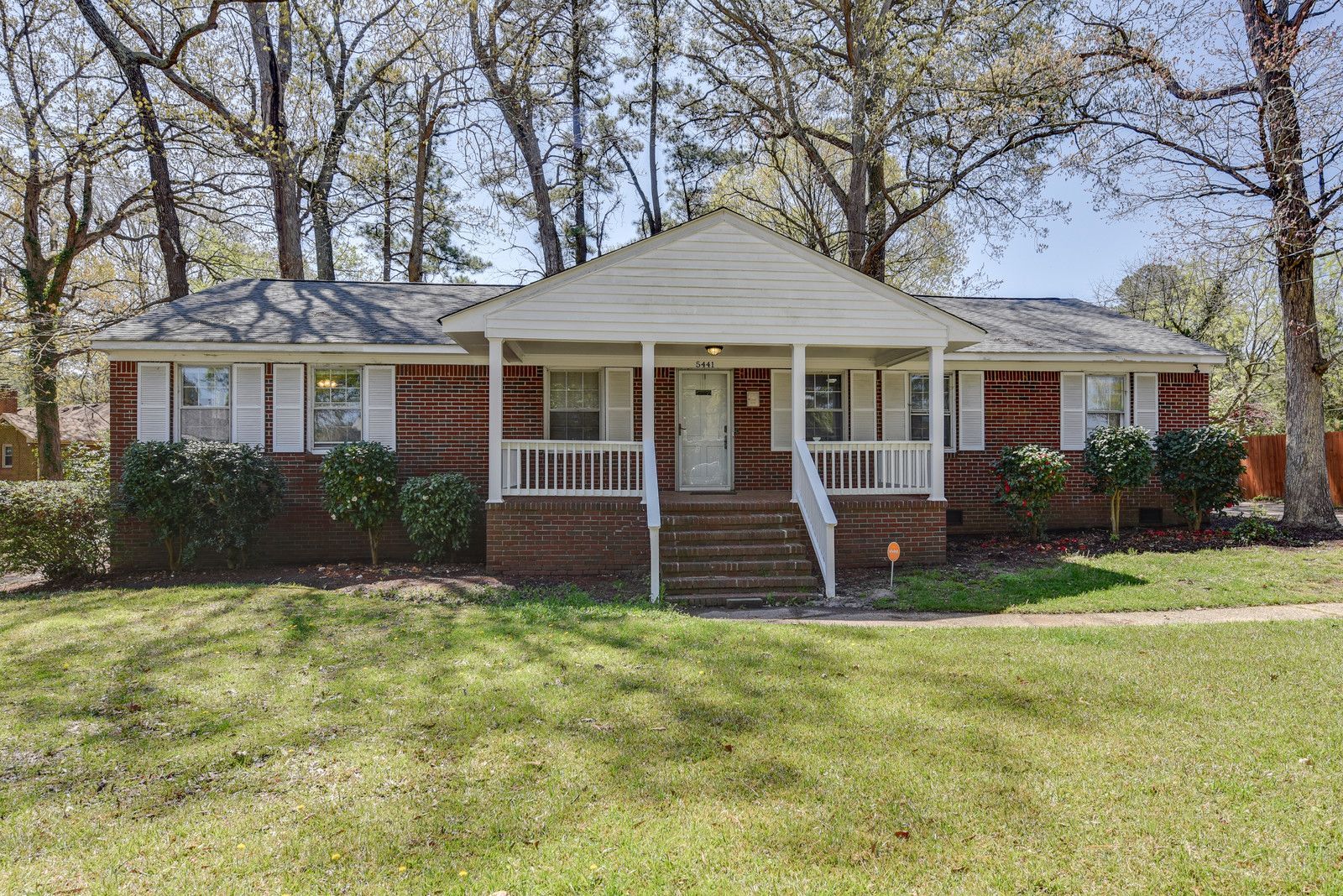 Single-story brick house with a front porch, white columns, and a large grassy yard.