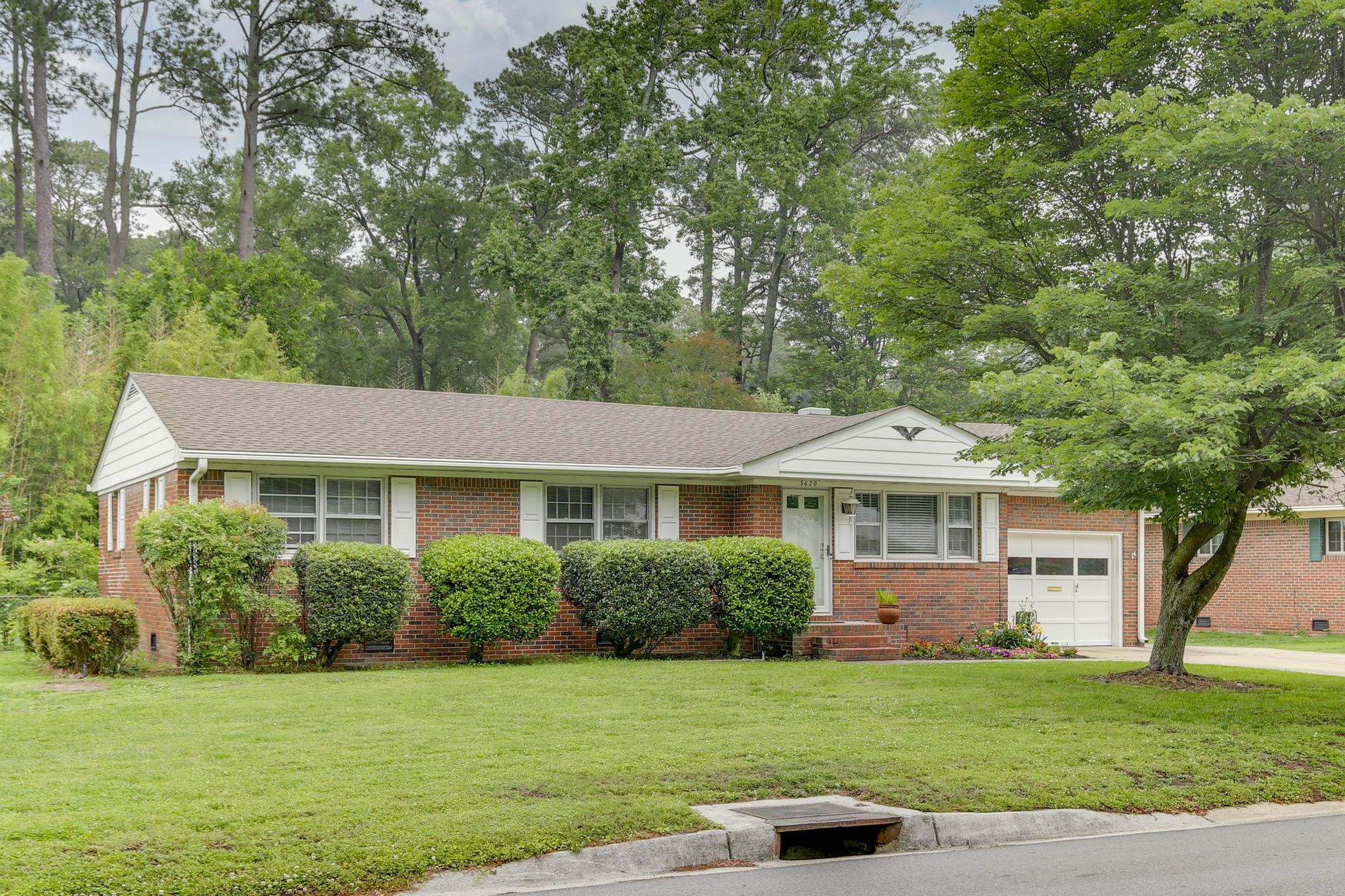 Single-story brick house with white trim, front porch, and a garage on a tree-lined suburban street