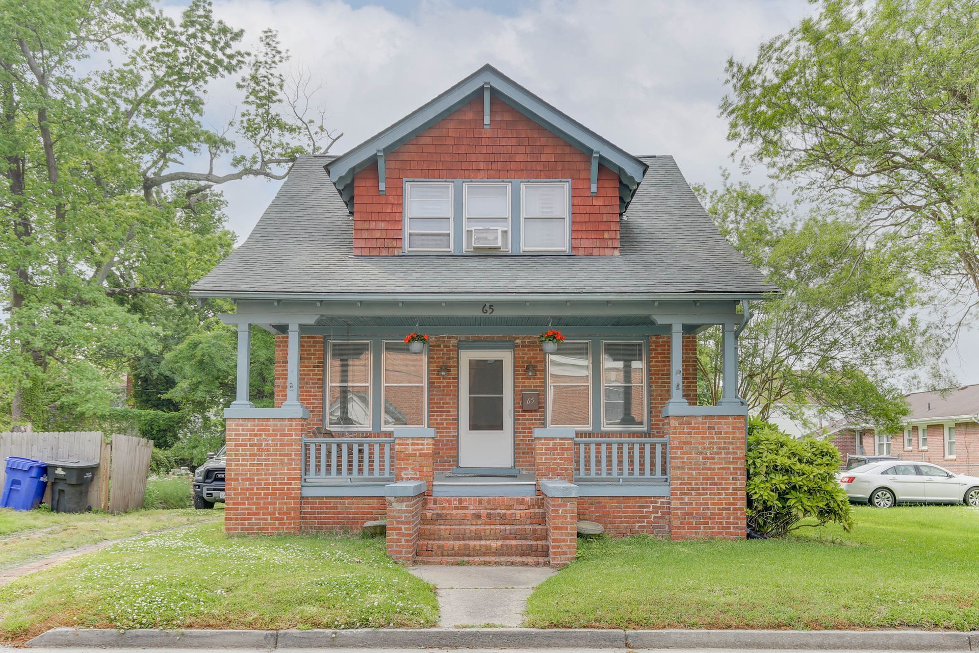 Brick house with a front porch and gray roof, framed by trees and a lawn.