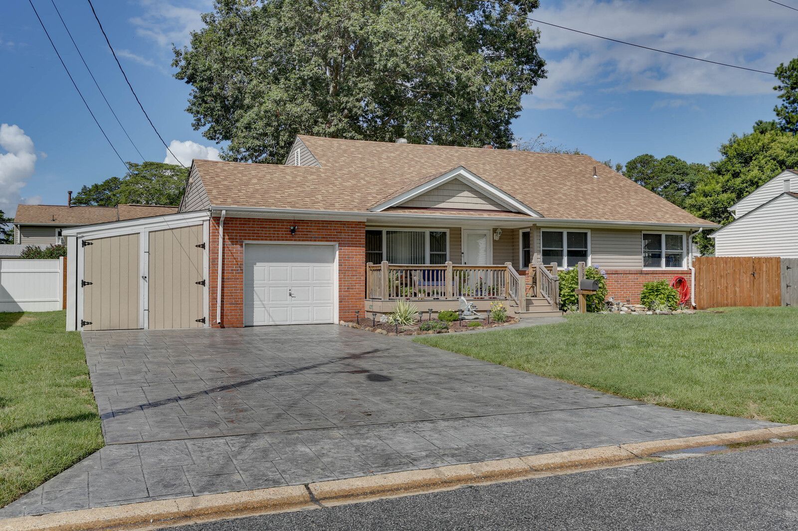 Single-story suburban house with attached garage, driveway, front porch, and lawn on a sunny day