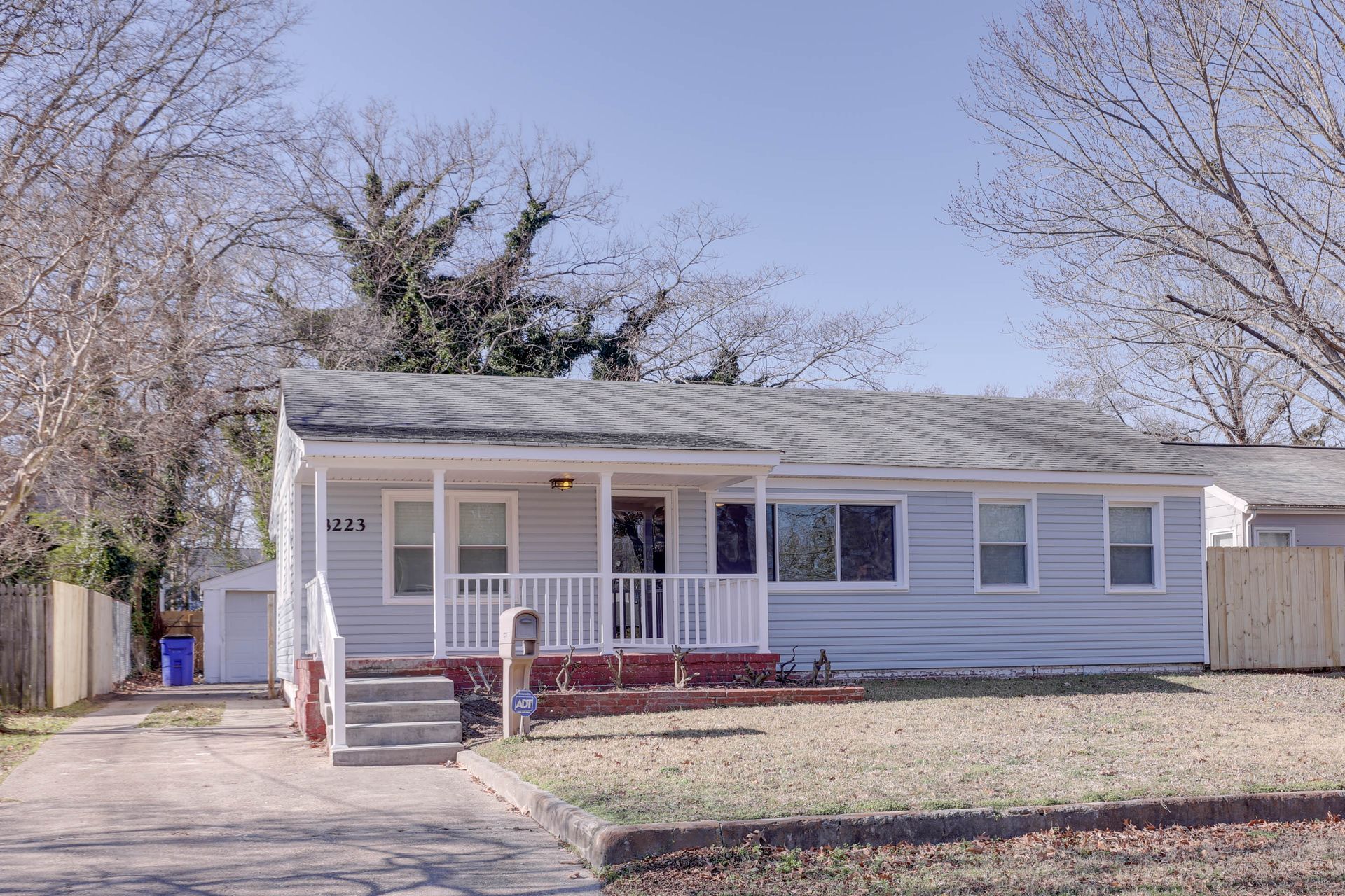 Single-story gray house with a white porch, red bench, and leafless trees in the yard