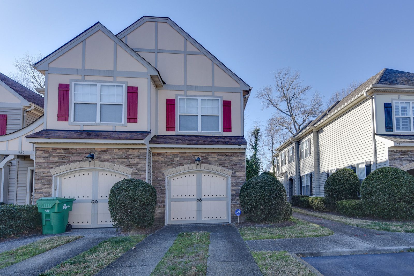 Suburban townhouse with two garage doors, red shutters, and a snow-covered front yard