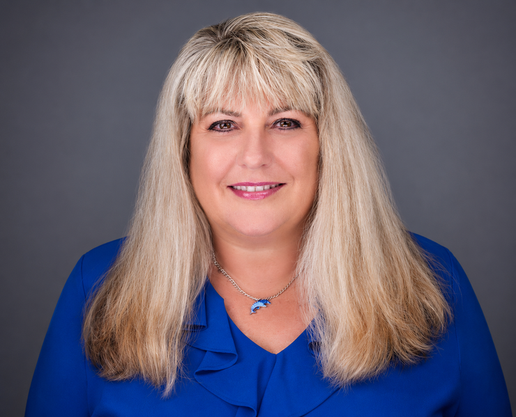 Smiling woman with long blonde hair wearing a blue blouse against a gray background