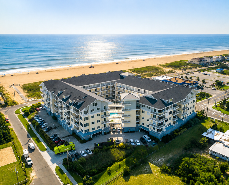 Aerial view of a beachfront resort with a large white building, parking lot, and ocean shoreline.