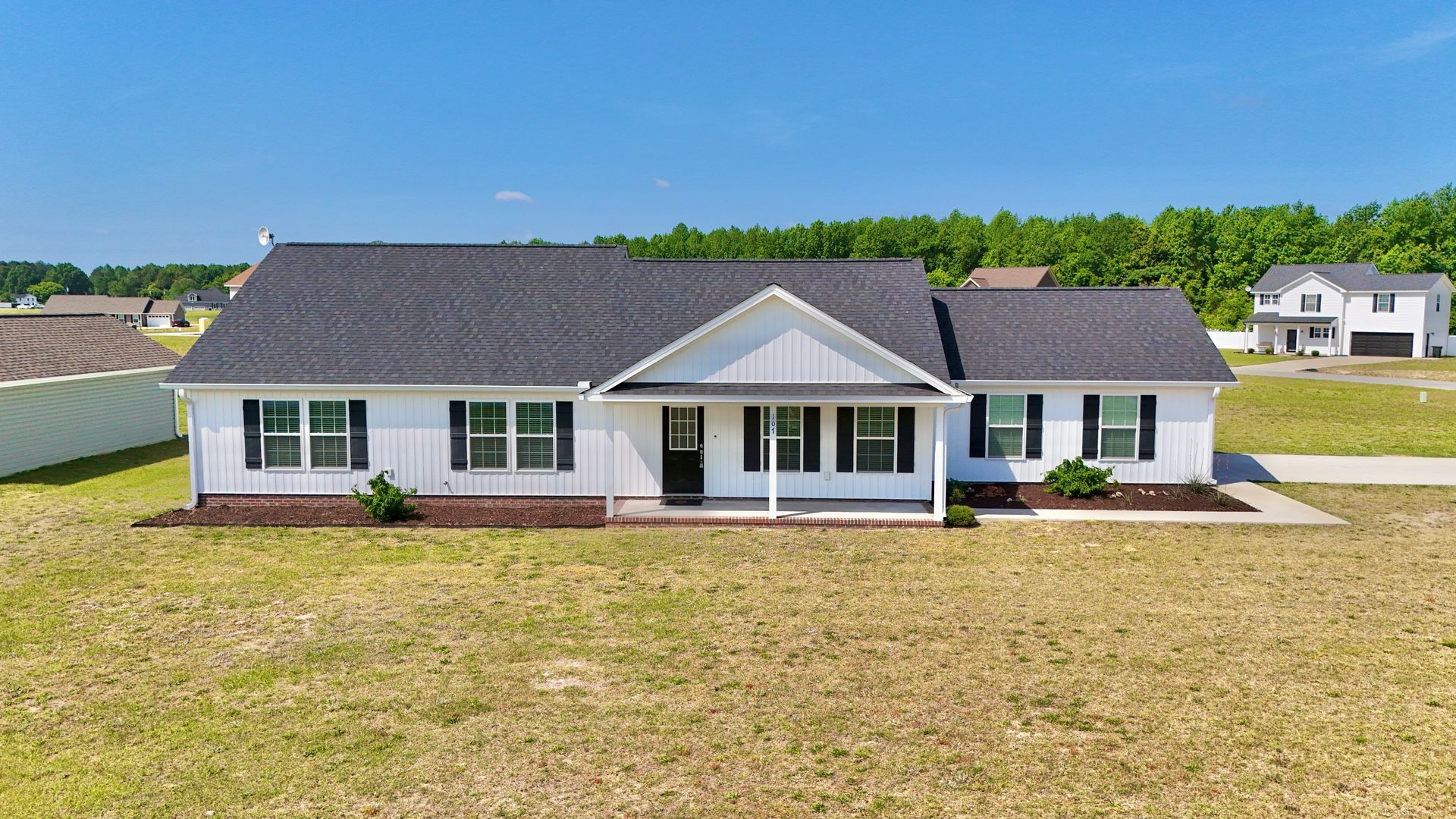 Single-story white house with dark roof and front porch in a grassy suburban lot