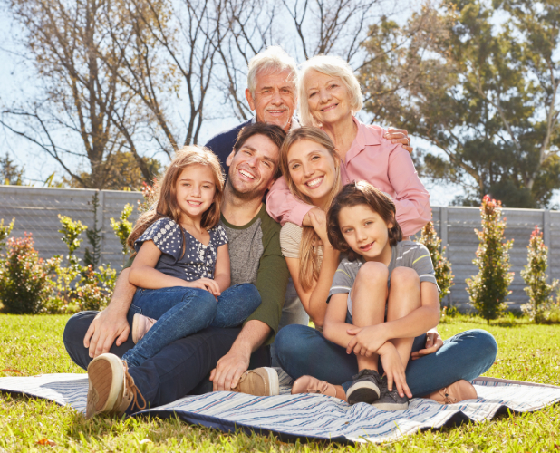 Family sitting together on a blanket in a sunny park, smiling with trees in the background