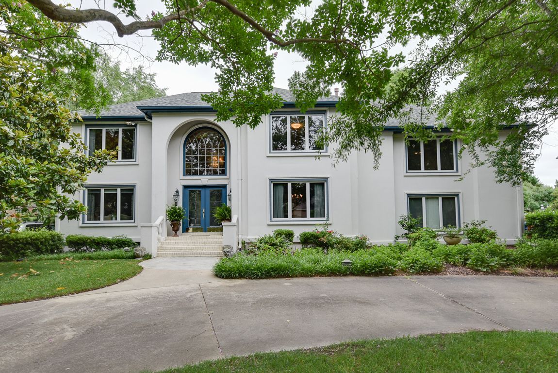Large white two-story house with arched entry, front steps, and trees overhead