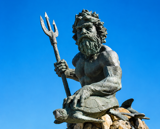Bronze sea god statue with trident seated on rocks against a blue sky