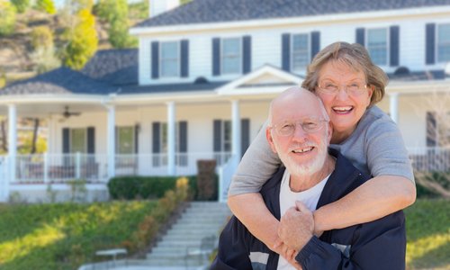 Smiling couple embracing in front of a white house with a porch and steps