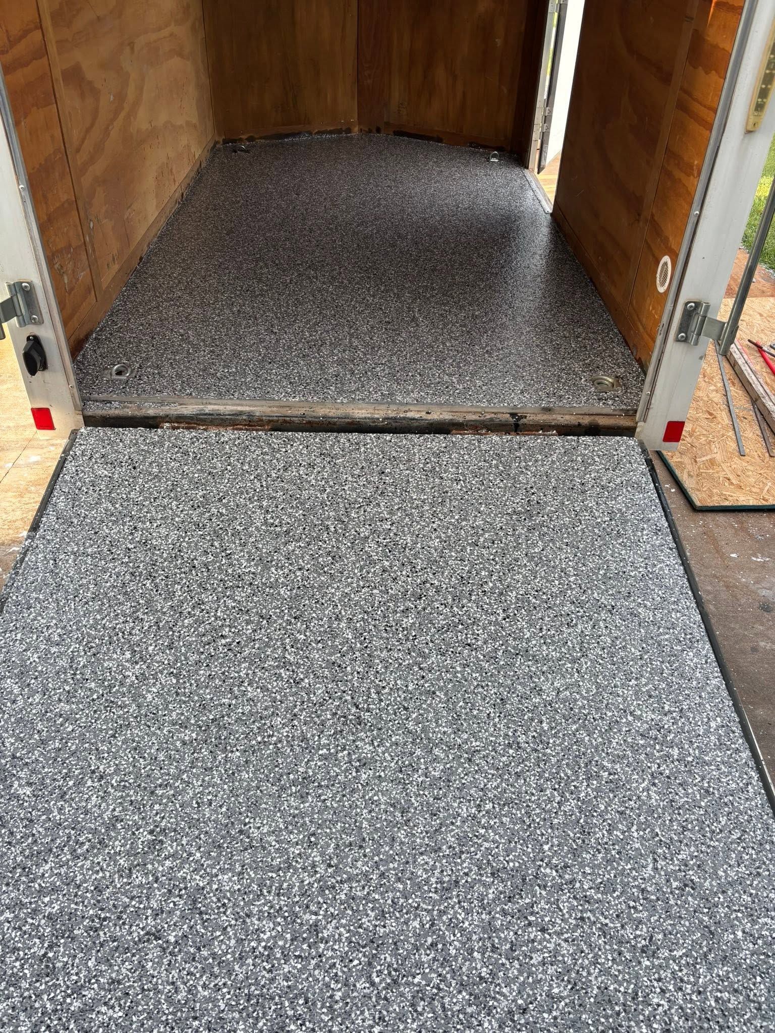 Wooden trailer doorway with a speckled gray carpeted ramp leading inside