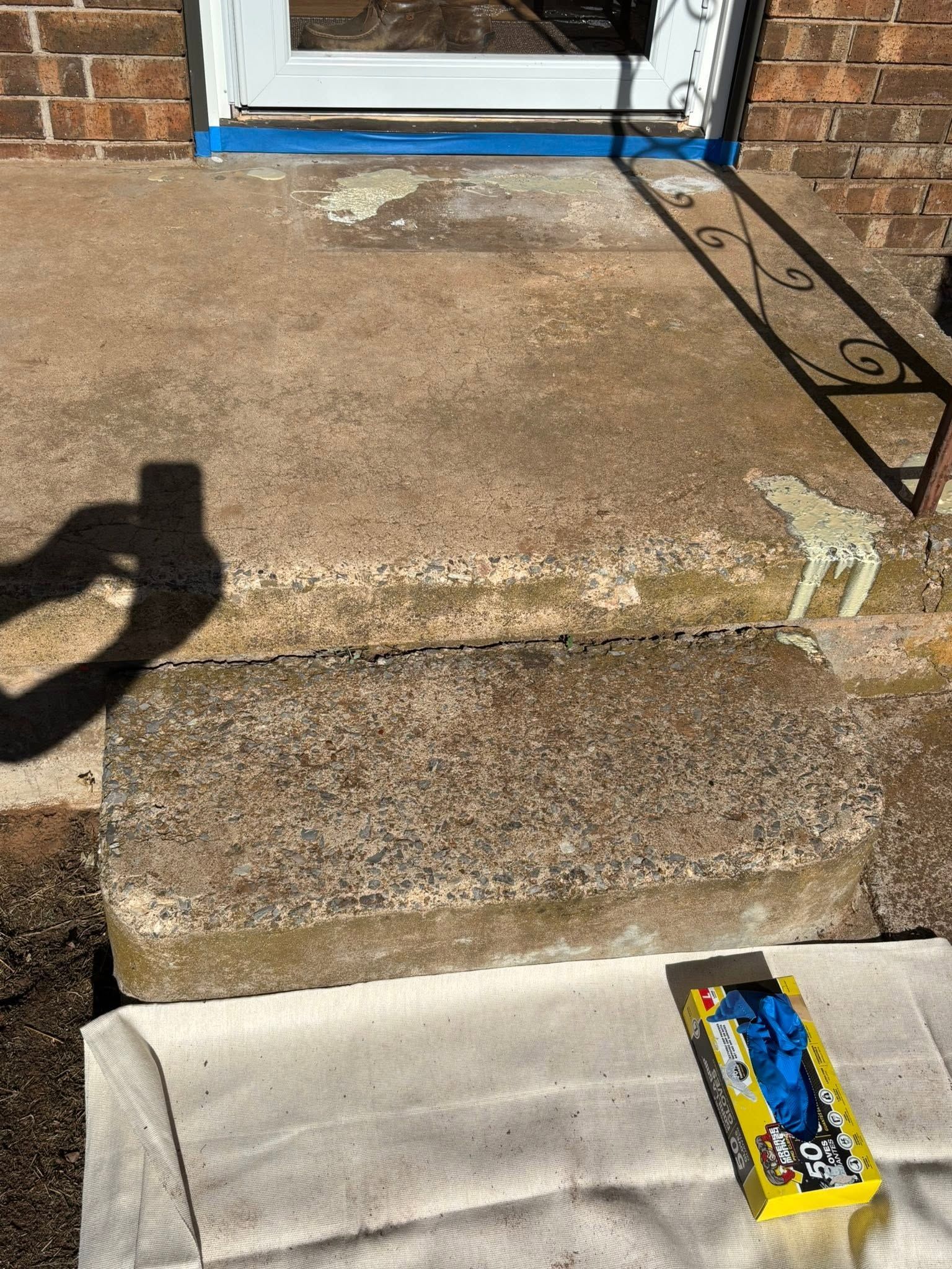Sunlit concrete steps leading to a white door, with a yellow-and-blue package on the lower step.