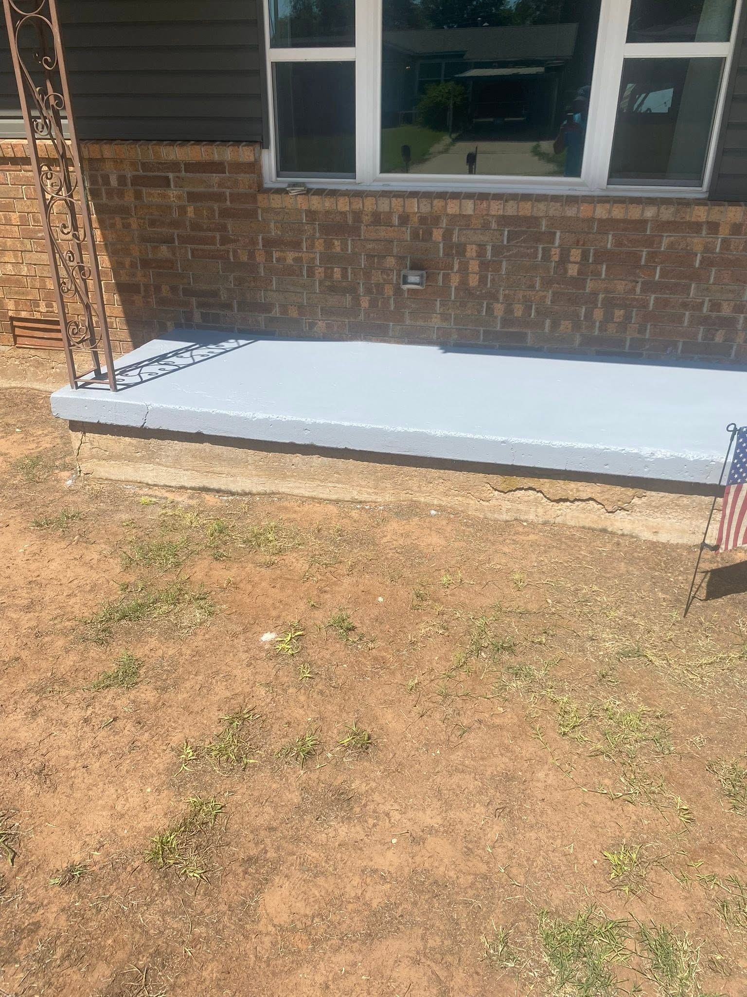 Concrete porch slab against a brick house wall with a window above a dirt yard.