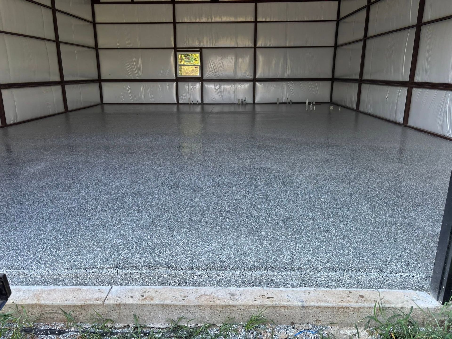 Empty metal garage interior with a gray speckled floor and a small window at the back.