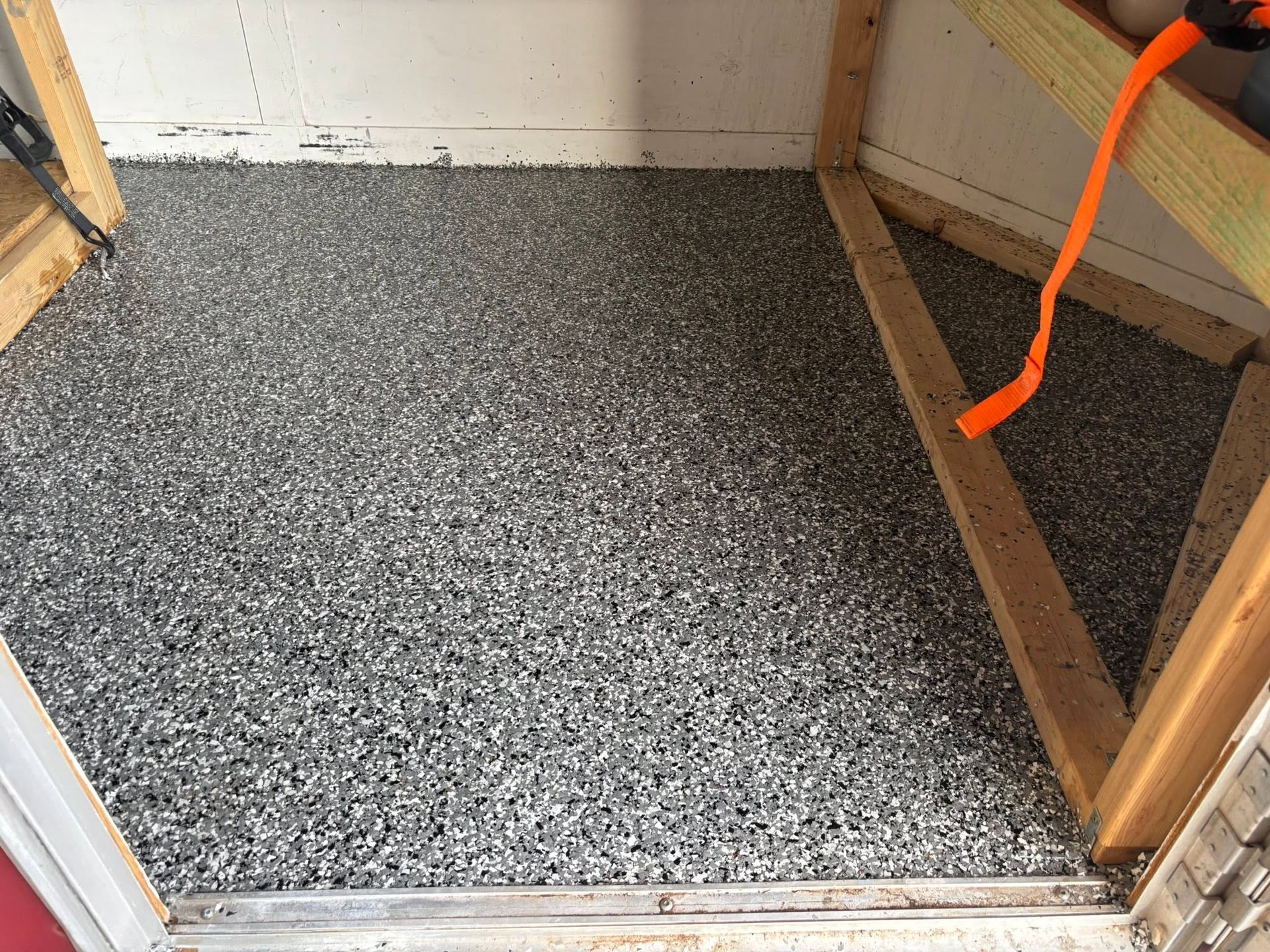 Open doorway to a room with speckled gray flooring and an orange strap on the right side