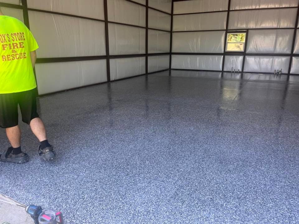 Empty metal garage with speckled epoxy floor; a person stands at left in a neon shirt.