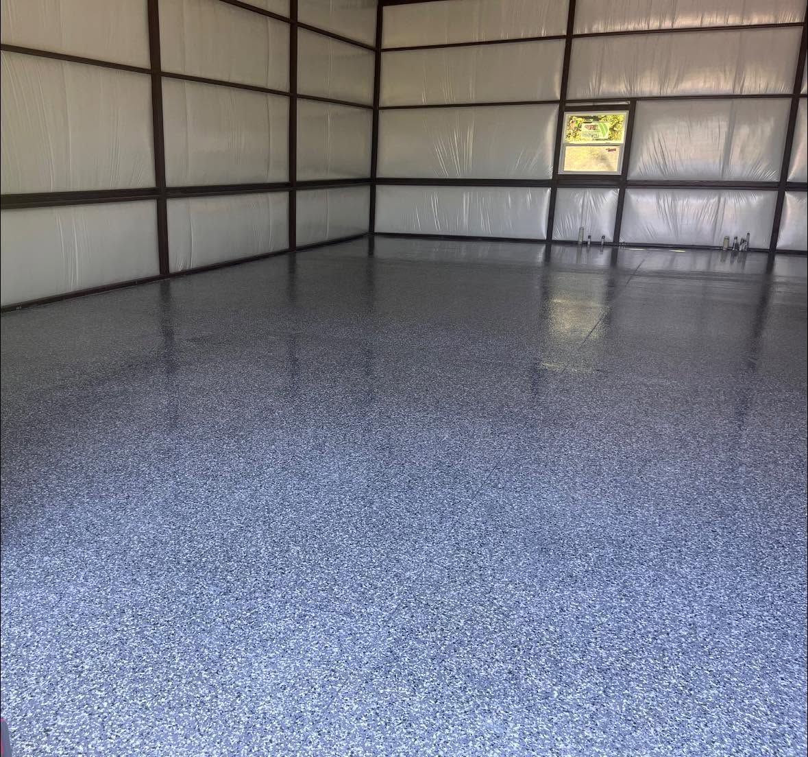 Empty metal building interior with a glossy speckled floor and a small window letting in light