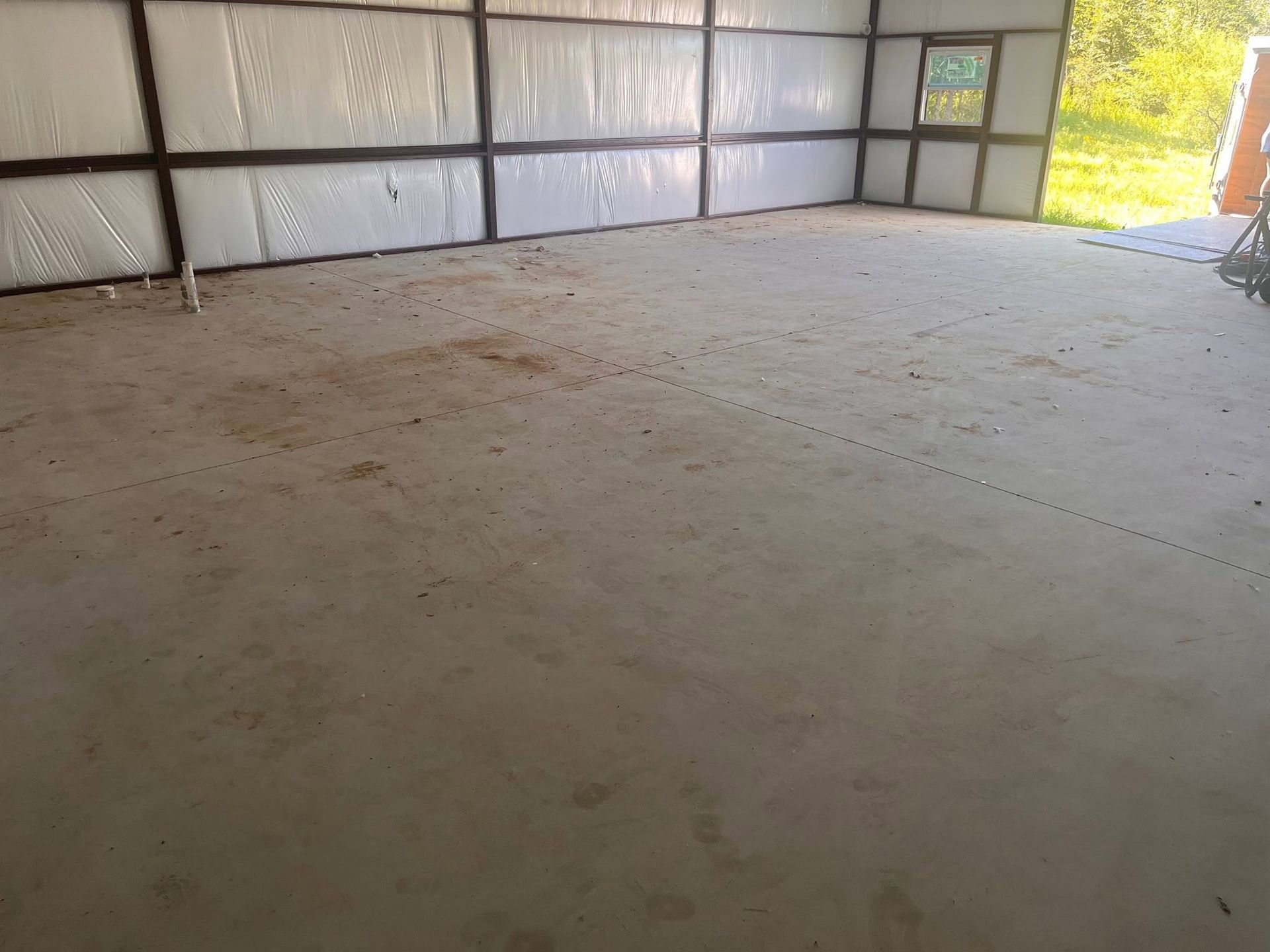 Empty unfinished metal building with a concrete floor and open doorway letting in daylight