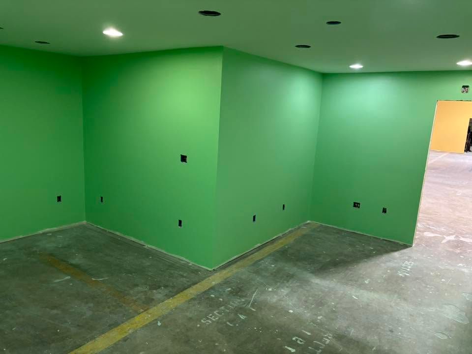 Empty green-walled room with unfinished concrete floor and recessed ceiling lights