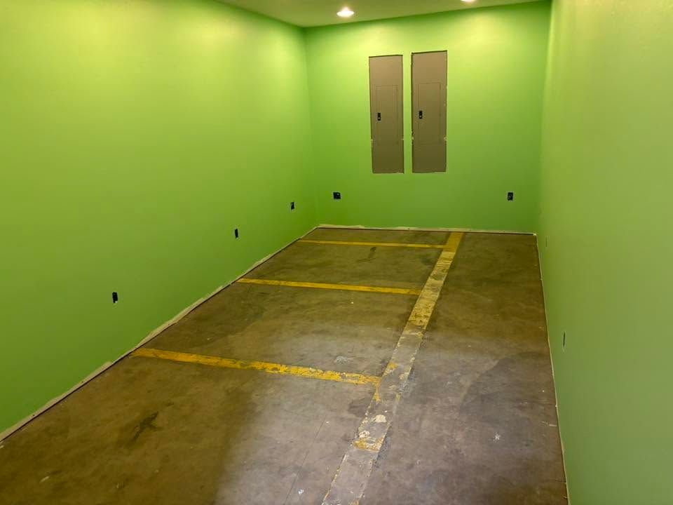 Empty lime-green room with concrete floor, yellow parking lines, and two narrow wall doors at the far end