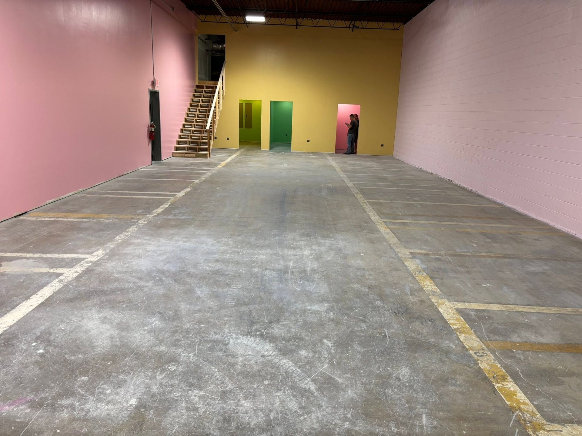 Empty indoor warehouse with pink and yellow walls, concrete floor, and a ladder near the back.