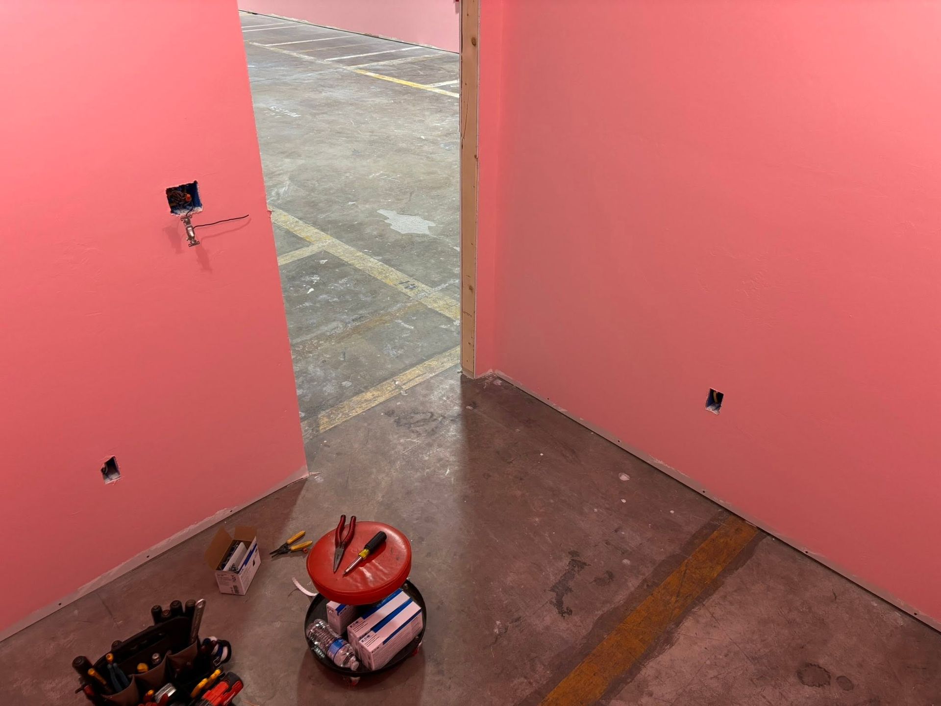 Open pink double doors onto a concrete area; tools and a bag lie on the floor inside.
