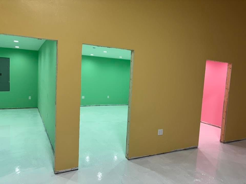 Empty room with tan walls, mint-green floors, green doorways, and a pink-lit doorway on the right
