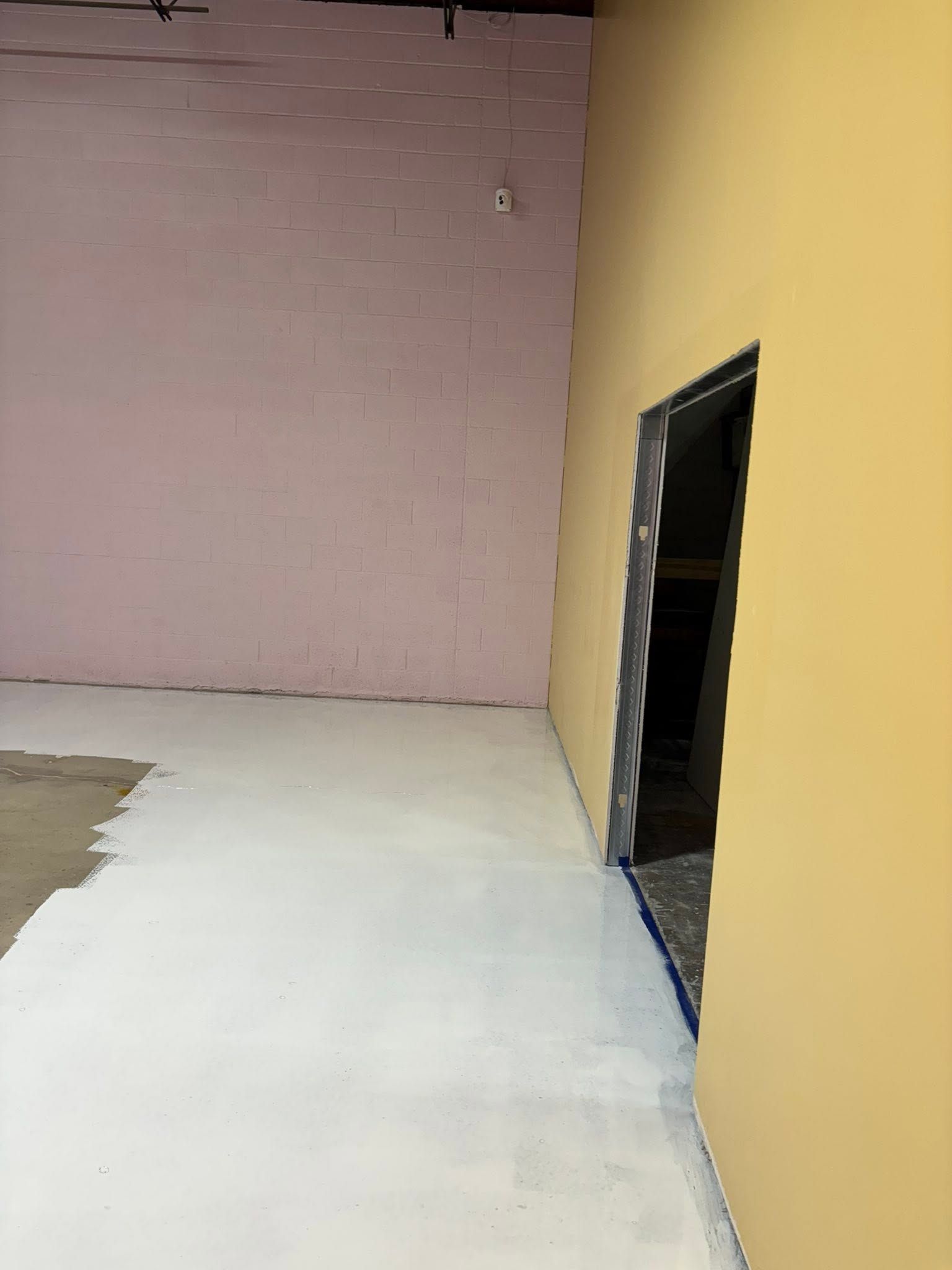 Empty room with pink and yellow walls, white floor, and a dark open doorway on the right.