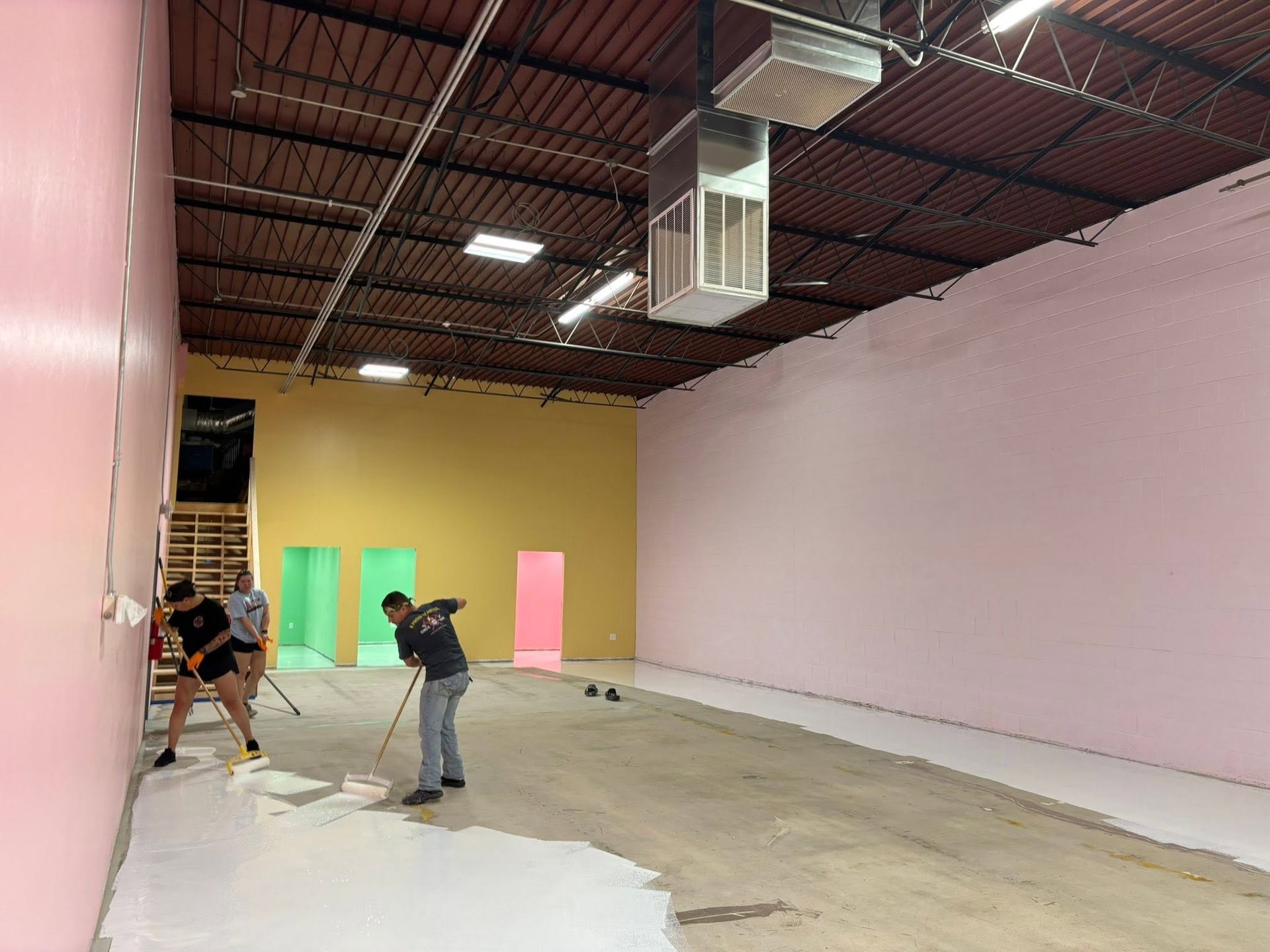 Two workers painting a large empty room with pink and beige walls