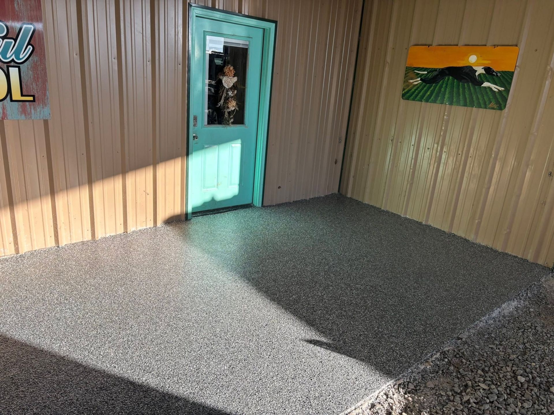 Sunlit storefront entrance with turquoise door, brown siding, and speckled concrete patio.