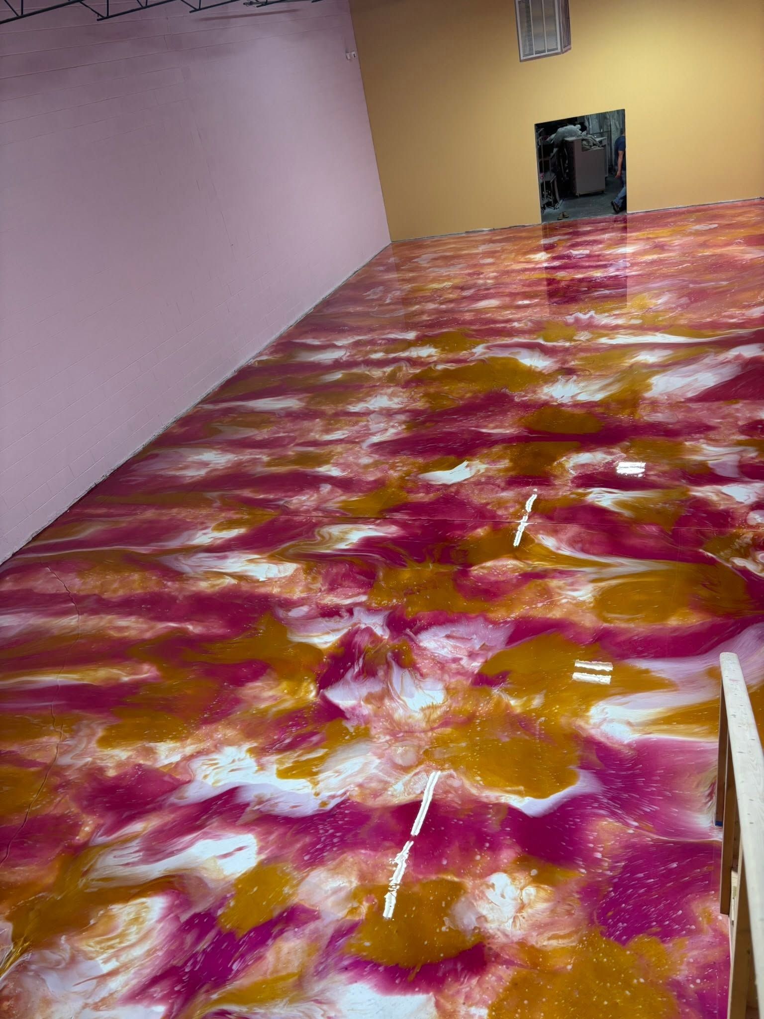 Empty room with pink walls and a yellow wall, featuring a colorful pink, orange, and white patterned floor.