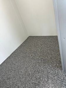 Small empty corner with white walls and a speckled gray floor inside a room or stall