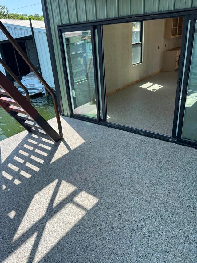 Covered patio with sliding glass doors, speckled flooring, and sunlight casting shadows.