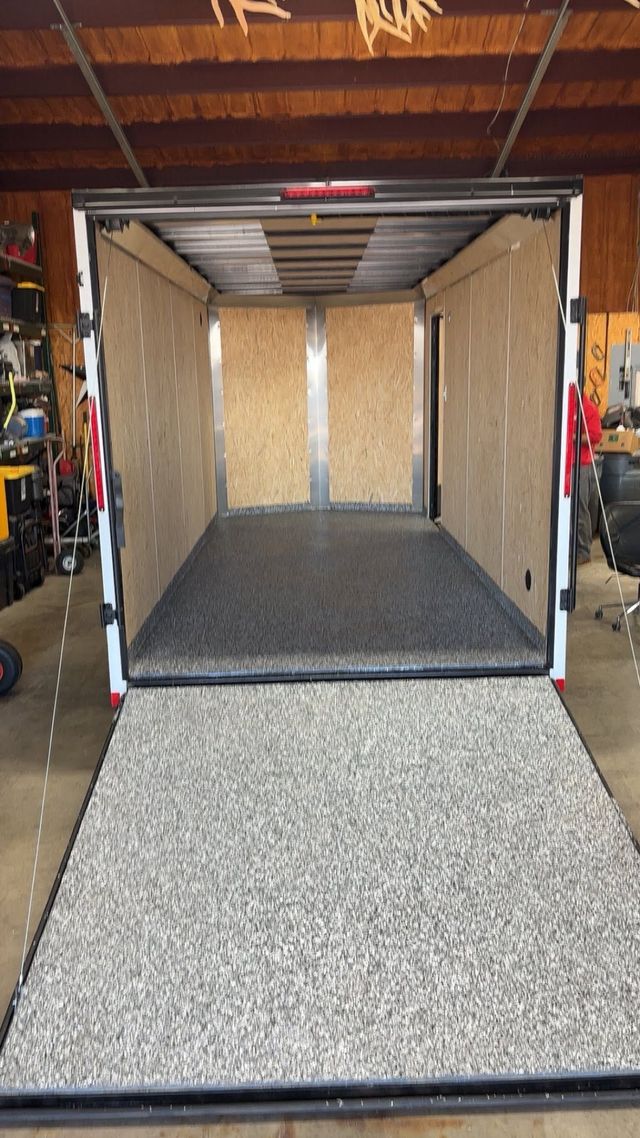 Open utility trailer with gray carpeted floor and beige walls in a garage.