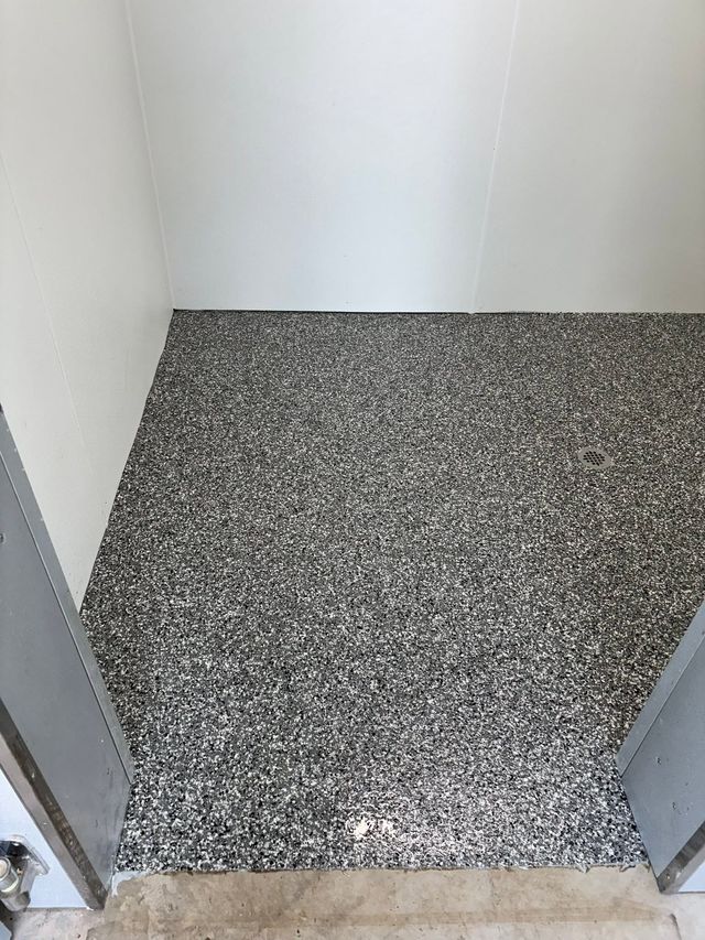 Small empty room with speckled gray floor and white walls, viewed from the doorway.