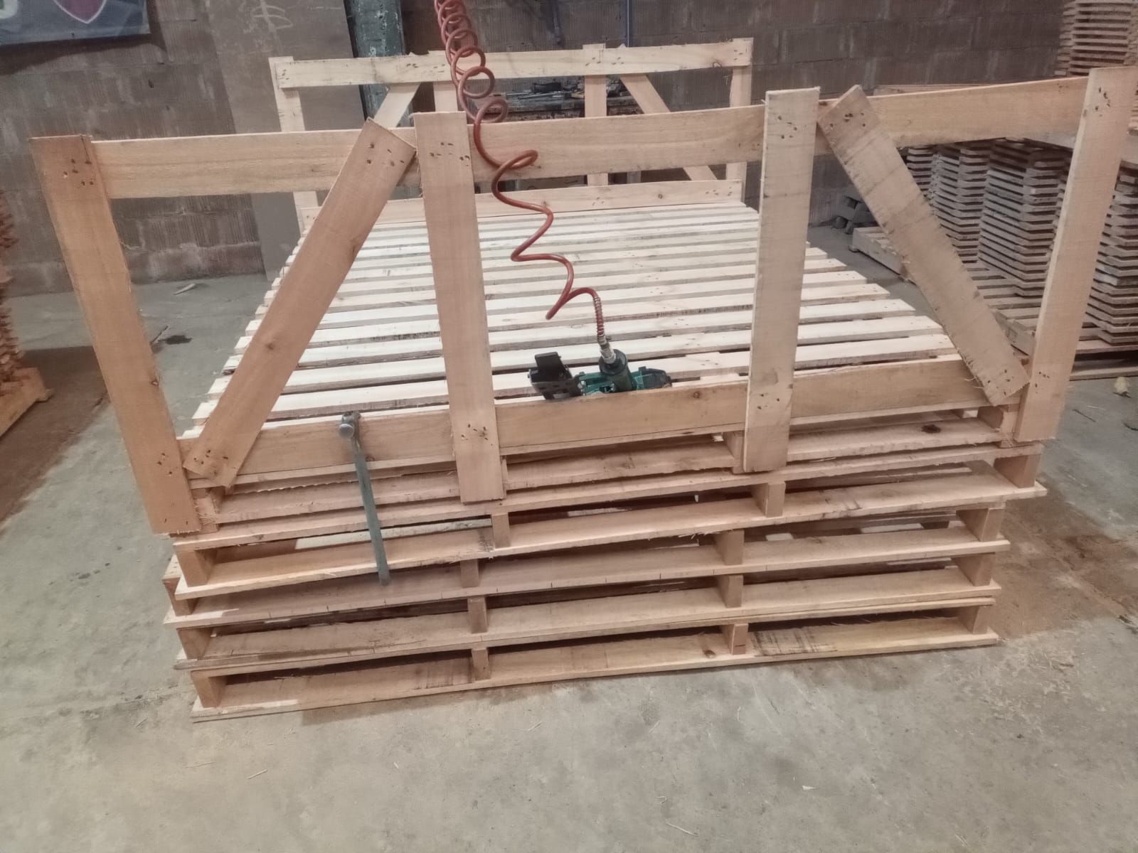 Estructura de cama de palets de madera en taller, con estructura de soporte y herramienta neumática.