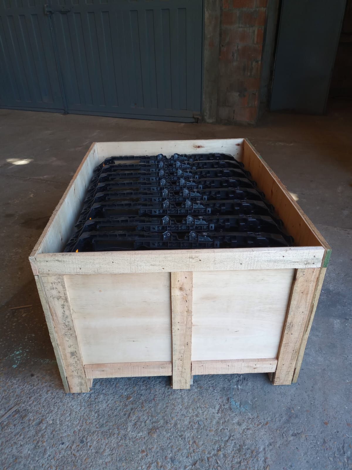 Una caja de madera para transporte, llena de piezas metálicas negras 