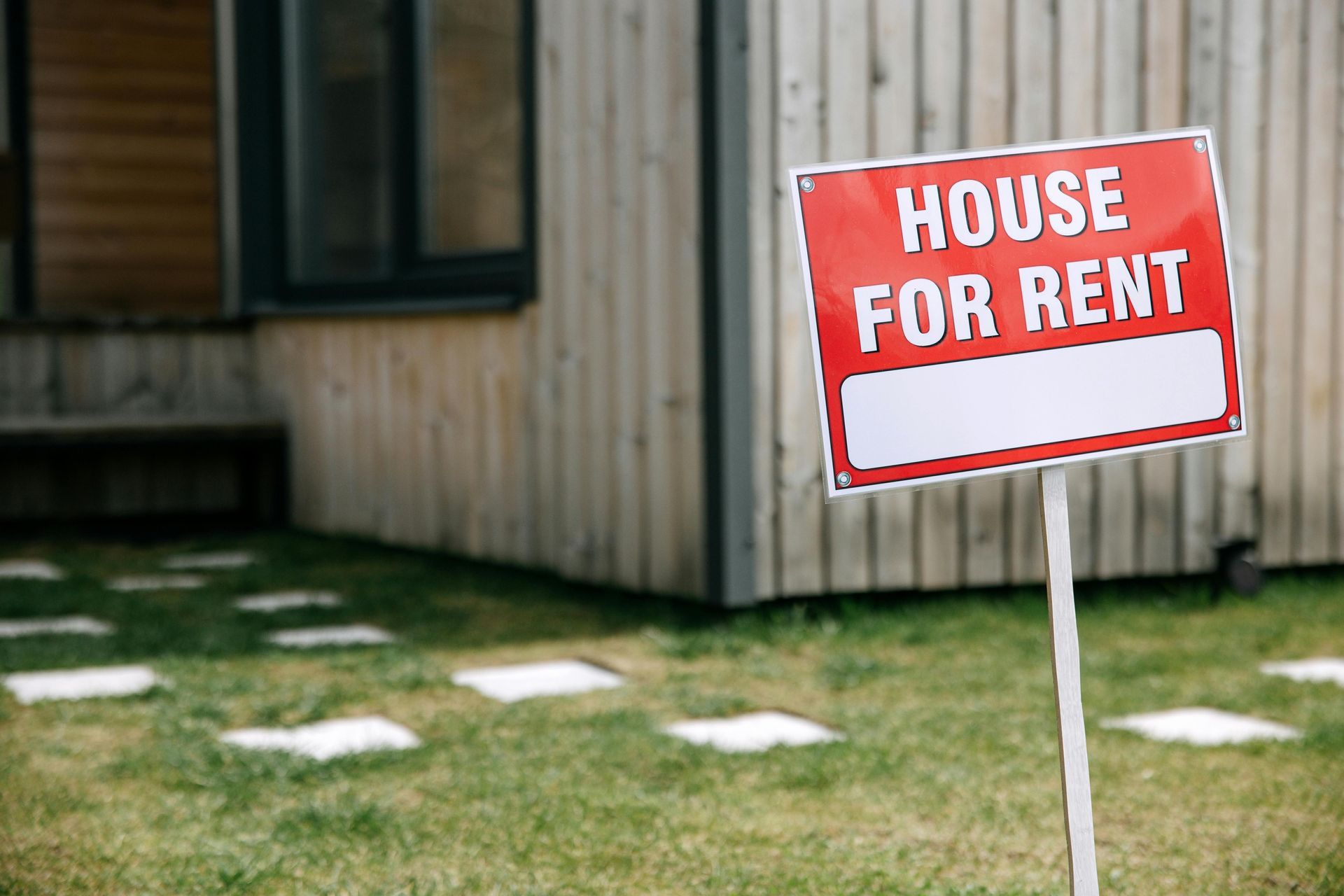 A house for rent sign is in front of a house.