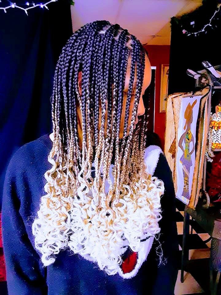 A woman with braids and curly hair is wearing a black sweater.