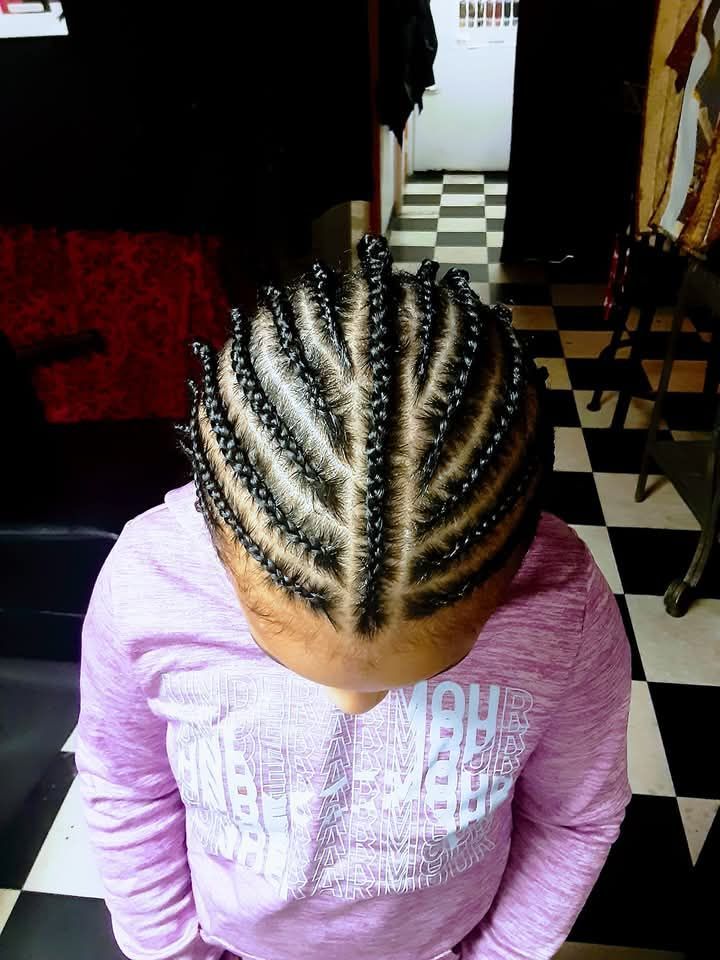 A little girl with braids on her head is wearing a pink shirt.